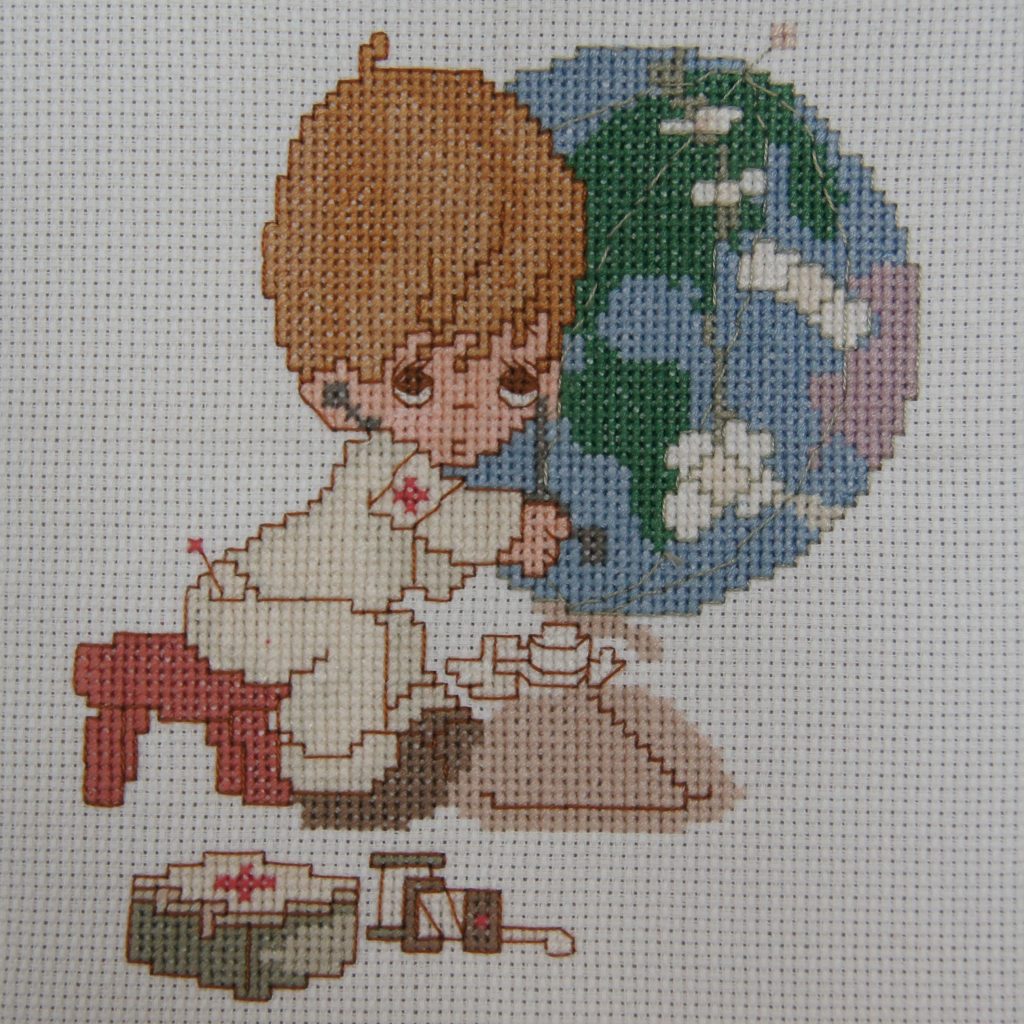 Photo of a cartoon-style cross stitch of a medic tending to a globe of the world